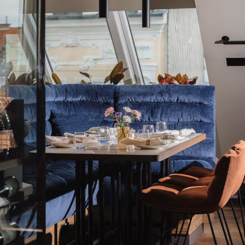Elegant gedeckter und mit Blumen geschm&uuml;ckter Tisch im WILMA Rooftop, direkt unter einem hellen Dachfenster.