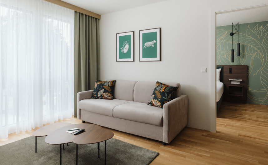 A spacious living room with a sofa, decorative artwork and views of the outdoor area and bedroom.